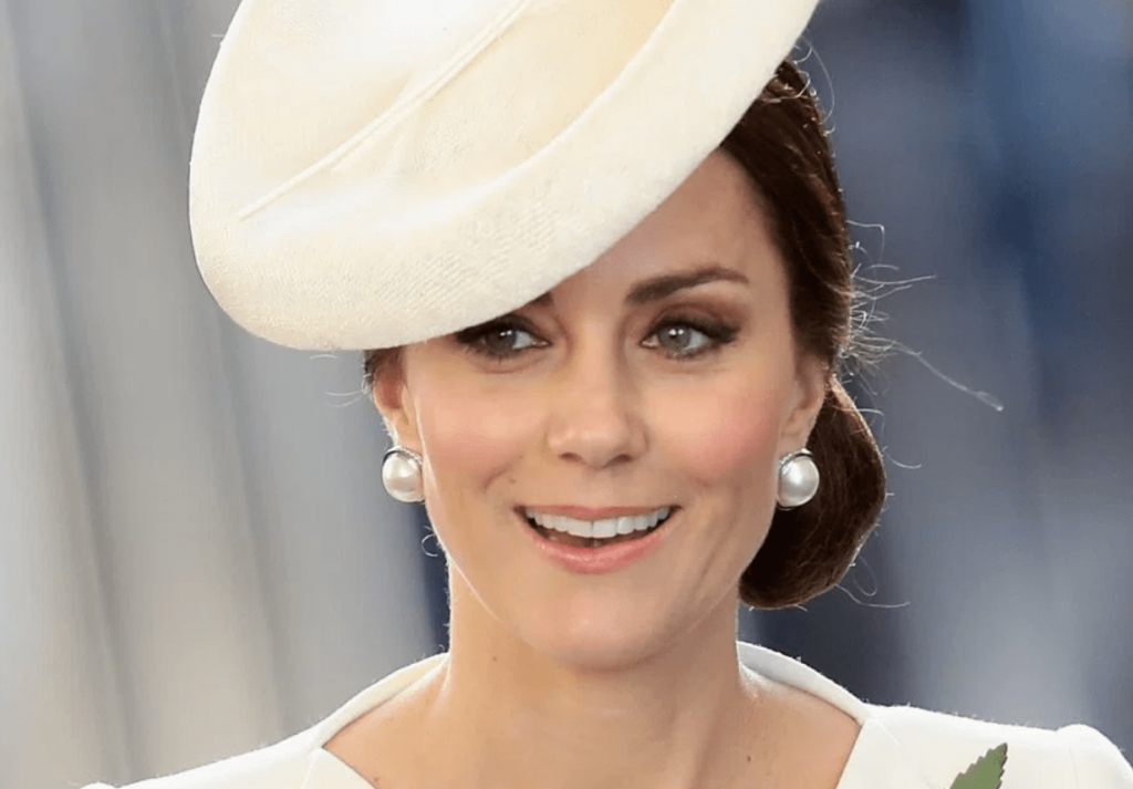 Kate Middleton usando brincos de pérolas e chapéu branco em um evento público.
