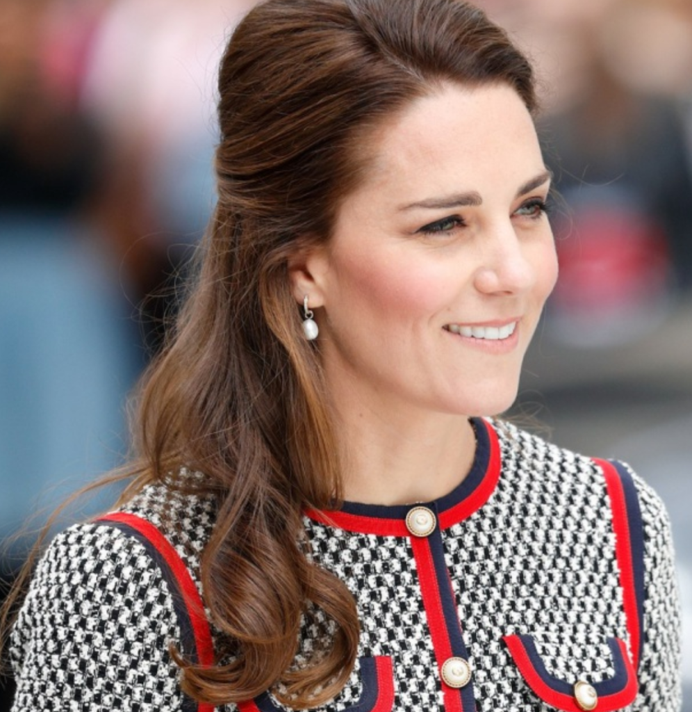 Kate Middleton sorrindo enquanto usa brincos de pérolas em um evento.