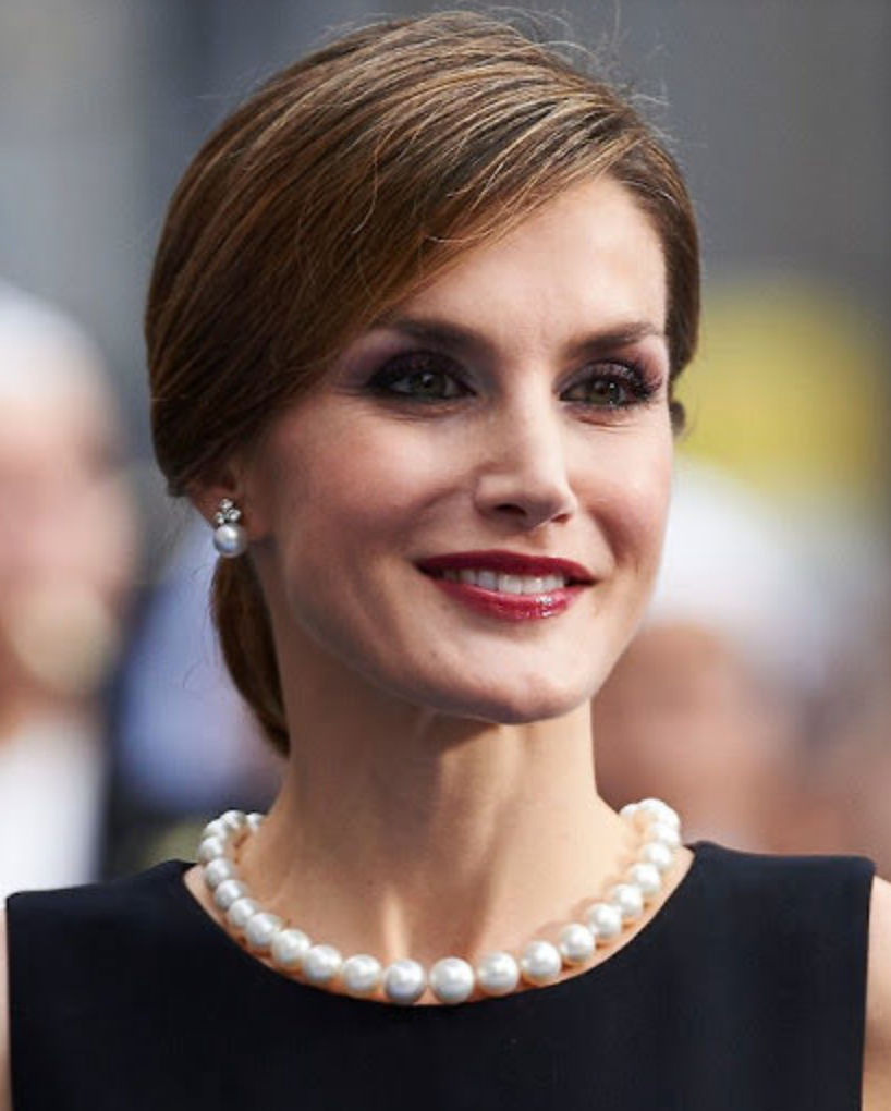 Rainha Letizia da Espanha sorrindo enquanto usa um colar e brincos de pérolas.