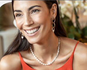 Mulher sorrindo, usando um colar de pérolas e brincos sofisticados, ideal para celebrações especiais.