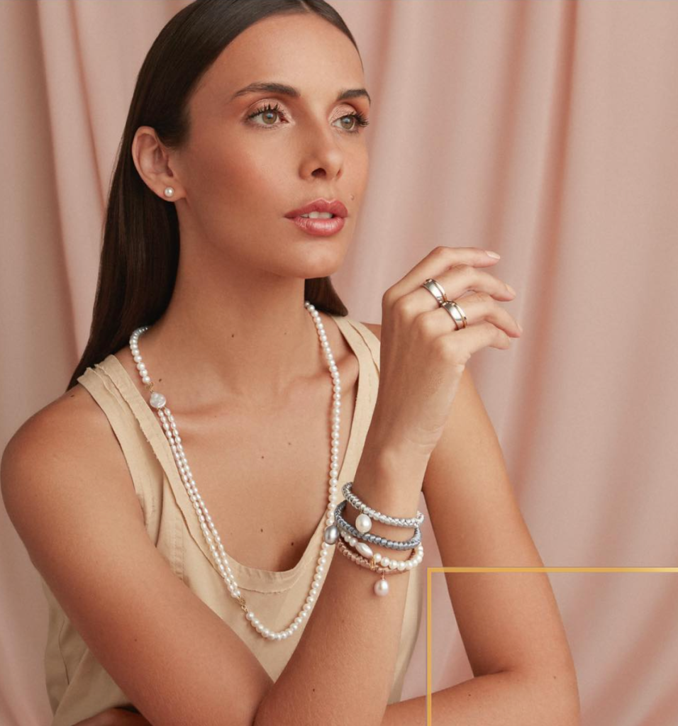 Mulher elegante usando mix de joias de pérolas, incluindo colar longo e pulseiras com design sofisticado e moderno.