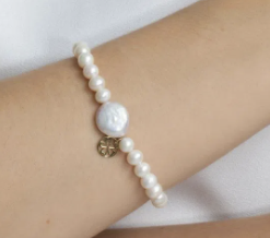Pulseira de pérolas creme com pingente dourado em pulso feminino