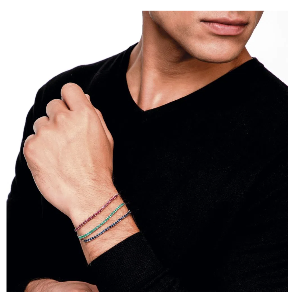 Homem usando conjunto de pulseiras Riviera em ouro branco com rubis, safiras e esmeraldas.